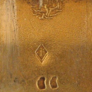 May include: Close-up of a textured, golden-colored surface with a diamond-shaped mark and two oval marks. The surface has a slightly aged appearance, with visible wear and tear.