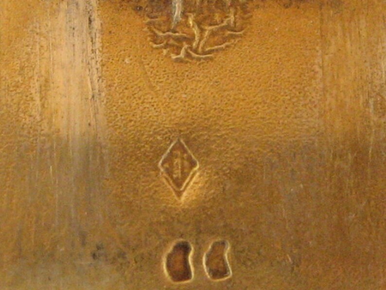 May include: Close-up of a textured, golden-colored surface with a diamond-shaped mark and two oval marks. The surface has a slightly aged appearance, with visible wear and tear.
