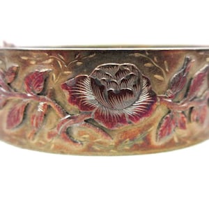May include: A vintage, ornate bracelet with a floral design. The bracelet is made of a metallic material with a reddish-brown and gold finish. The design features a large rose and leaves.