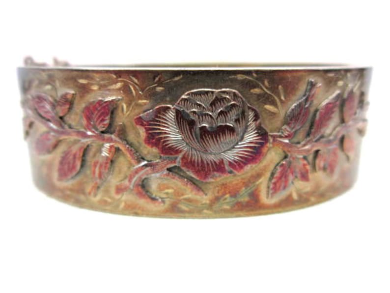 May include: A vintage, ornate bracelet with a floral design. The bracelet is made of a metallic material with a reddish-brown and gold finish. The design features a large rose and leaves.