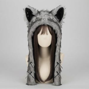 May include: A grey and black faux fur hood featuring large animal ears with silver studs, a delicate silver chain draped across the forehead with small heart charms, and long side panels accented with thin black ribbon bows on each side.