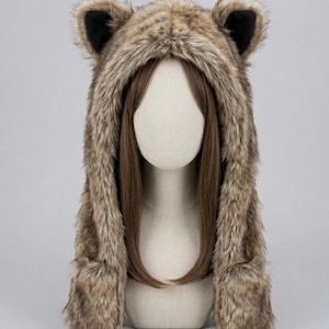May include: A faux fur hood featuring a brown and tan animal-inspired pattern with two upright ears on top. The hood has long side panels that hang down, and the interior of the ears is lined with black fabric. The hood is displayed on a mannequin.