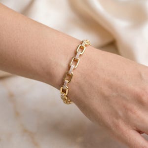 Puede incluir: Una pulsera de eslabones dorados con forma rectangular. Cada dos eslabones, uno está adornado con una fila de pequeñas piedras claras y brillantes en la superficie exterior, creando un patrón repetitivo de eslabones dorados y con piedras.