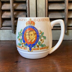 May include: White ceramic mug with a royal blue and gold crest featuring a portrait of King George VI and Queen Elizabeth. The crest includes the text "Honi Soit Qui Mal Y Pense" and "Dieu Et Mon Droit".