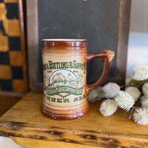 May include: A brown ceramic beer stein with a green and white label that reads "Dove Brand Ginger Ale" and "Virginia Bottling & Supply Co. Trade Mark". The stein has a handle shaped like a bird.