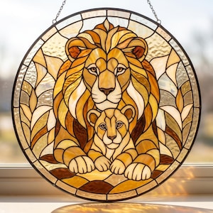 May include: A circular stained glass panel featuring a lion and a cub in shades of amber, gold, and brown. The design uses dark lead lines to define the feline features and surrounding foliage patterns, suspended by a metal chain for display.