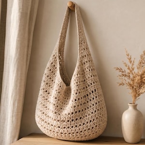 Può includere: Una borsa hobo all'uncinetto color beige caratterizzata da un motivo traforato con un unico spallaccio integrato. La borsa è realizzata in filato di colore chiaro e presenta una silhouette arrotondata e morbida con un motivo a punti ripetuto.