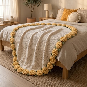 May include: A cream-colored, crocheted blanket with a circular design, draped over a bed. The blanket is trimmed with yellow rose appliques and green leaves. The bed has yellow and cream-colored pillows.