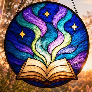 Puede incluir: Un atrapasoles circular de vidrieras que muestra un libro abierto en la parte inferior con luz emanando hacia arriba en patrones ondulados de azul, morado y turquesa, acentuado por estrellas amarillas sobre un fondo azul oscuro, colgado de una cadena.