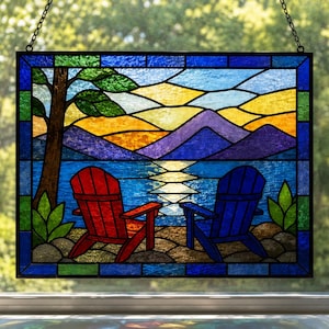 Könnte beinhalten: Ein rechteckiges Buntglas-Fensterbild mit einer Landschaftsszene, die einen roten und einen blauen Stuhl an einem felsigen Ufer zeigt. Das Motiv umfasst einen See, violette Berge, einen gelben Sonnenuntergangshimmel und einen Baum, umrahmt von einer blau-grünen Bordüre.