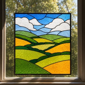 May include: A square stained glass panel featuring a landscape of rolling green and yellow hills under a blue sky with white clouds. The scene is composed of textured glass pieces held together by dark lead lines, hanging by a metal chain.