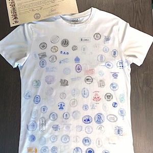 Può includere: T-shirt bianca con numerosi disegni di timbri colorati. La maglietta ha un girocollo e maniche corte. Un documento con bordi ornati e testo è visibile sullo sfondo. La maglietta ha la scritta "JACK PARKER" sul colletto.