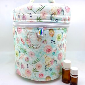 Puede incluir: Una bolsa redonda de tela con estampado floral, cremallera y asa. La bolsa está llena de pequeñas botellas de vidrio ámbar con tapas blancas. La bolsa es perfecta para guardar aceites esenciales.