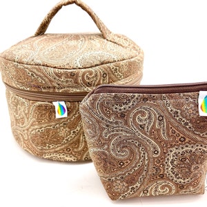May include: Two paisley-patterned cosmetic bags. One is a round, handled case with a zipper, and the other is a smaller, trapezoid-shaped pouch. Both are in shades of brown and tan, with a rainbow logo tag.