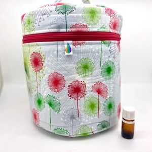 Peut inclure: Un contenant de rangement rond en tissu gris avec une fermeture éclair rouge et un imprimé de pissenlits. Le contenant est rempli de bouteilles d'huile essentielle.