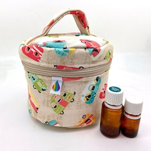 Peut inclure: Une trousse de transport d'huiles essentielles beige avec une poignée, ornée d'un motif de caravanes colorées. La trousse a une fermeture éclair et une étiquette logo arc-en-ciel. Deux petites bouteilles marron sont à côté.