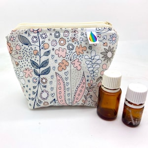 May include: A white zippered pouch with a floral print in shades of pink, gray, and blue. The pouch is filled with two small amber glass bottles with white caps.