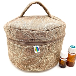 May include: A circular essential oil storage case with a paisley pattern in shades of brown, featuring a zip closure and a handle. Two small brown glass bottles and one with a white cap are next to the case. A rainbow logo tag is attached.