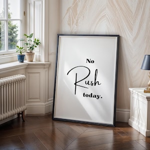 Może przedstawiać: Oprawiony wydruk artystyczny ze słowami "No Rush today" w czarnym skrypcie. Wydruk jest w czarnej ramie i opiera się o ścianę. Pokój ma okno, rośliny, mały stolik i lampę.