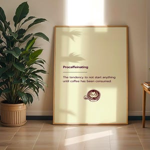 Puede incluir: Un póster enmarcado con la palabra "Procaffeinating" en una fuente burdeos oscuro. El póster tiene un fondo amarillo claro con el texto "La tendencia a no empezar nada hasta que se haya consumido café". Una ilustración de taza de café está en la parte inferior.