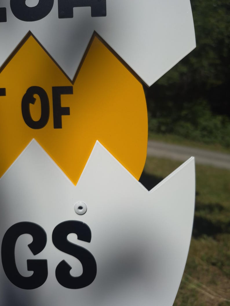 May include: A white and yellow sign shaped like a cracked egg. The white portion features black text with the letters GS visible at the bottom and the letters OF visible in the middle. The yellow center section is smooth and solid in color.