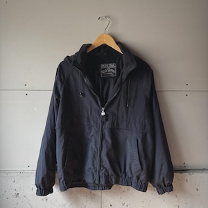 Puede incluir: Chaqueta negra con capucha, cierre de cremallera y dos bolsillos delanteros. La chaqueta está colgada de una percha de madera. El nombre de la marca "PACIFIC TRAIL" es visible en una etiqueta interior.