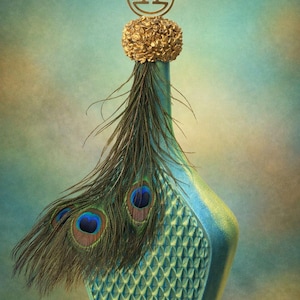 May include: A decorative teal bottle with a gold-colored stopper and a peacock feather accent. The bottle has a diamond pattern on the front and a gold emblem on top. The peacock feathers have blue and brown eye markings.