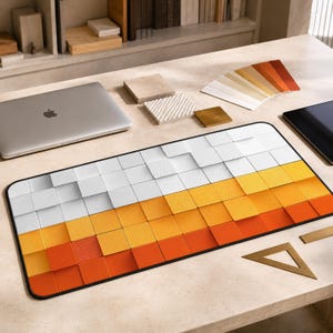 Peut inclure: Un tapis de bureau rectangulaire présentant un motif en dégradé de carrés passant du blanc au jaune puis à l'orange. La surface a un aspect texturé en blocs tridimensionnels avec un bord noir, conçu pour un espace de travail informatique.
