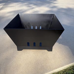 May include: A black, geometric fire pit with a square shape and angled sides. The fire pit has three rectangular cutouts on each side and sits on four small feet. Smoke is visible inside the pit.