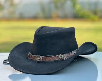 May include: A black hat with a wide brim and a pinched crown. The hat features a brown textured leather band around the base, decorated with evenly spaced circular metal conchos that have a radial pattern and a central stud detail.