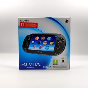Op de afbeelding: Een zwarte PlayStation Vita console doos. De doos toont een afbeelding van de console met een scherm met app-iconen. De doos toont ook het PS Vita-logo, het Sony-logo en 3G/Wi-Fi-informatie.