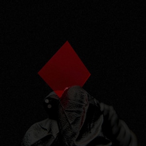 Puede incluir: Imagen abstracta con forma de rombo rojo sobre fondo negro. La parte inferior de la imagen muestra un objeto oscuro y texturizado, posiblemente tela o cuero, con dos pequeños círculos brillantes.