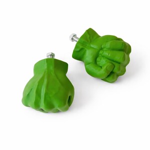 Op de afbeelding: Twee groene vuistvormige kastknoppen met zilveren bouten. De knoppen zijn felgroen en hebben gedetailleerde beeldhouwwerken die lijken op een gebalde vuist. Deze decoratieve knoppen zijn ideaal om een unieke touch aan meubels toe te voegen.
