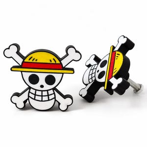 Può includere: Due pomelli decorativi per armadi con un design a teschio e ossa incrociate a cartoni animati. Il teschio indossa un cappello giallo con una fascia rossa. I pomelli sono neri, bianchi e gialli, con una vite argentata.