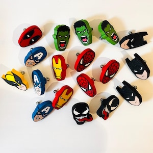 Può includere: Una collezione di pomelli decorativi per cassetti raffiguranti vari volti di personaggi dei fumetti, tra cui Deadpool, Hulk, Batman, Capitan America, Iron Man, Spider-Man, Wolverine e Venom, ciascuno con una vite di montaggio in metallo.