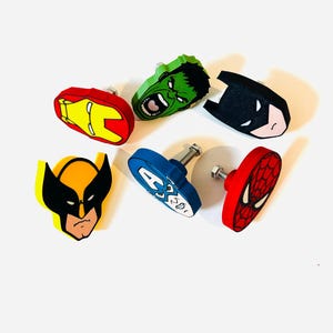 Op de afbeelding: Een verzameling van zes kleurrijke kastknoppen met superheldenontwerpen. De knoppen bevatten Iron Man, Hulk, Batman, Wolverine, Captain America en Spider-Man. Elke knop heeft een andere kleur en een metalen schroef voor installatie.