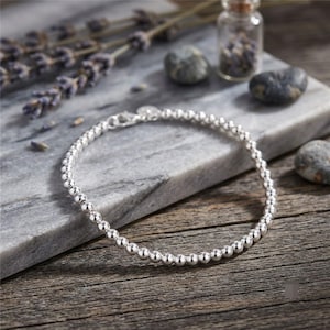 May include: A delicate bracelet composed of small, polished silver-toned spherical beads arranged in a continuous circular chain. The bracelet features a small metal lobster claw clasp mechanism for securing the ends together on the wrist.