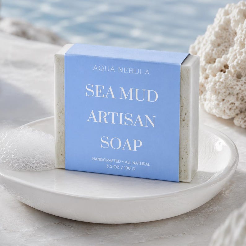 May include: A rectangular bar of off-white sea mud soap wrapped in a light blue paper band. The label features the text AQUA NEBULA, SEA MUD ARTISAN SOAP, HANDCRAFTED, ALL NATURAL, and 3.5 OZ / 100 G in white, sans-serif and serif fonts.