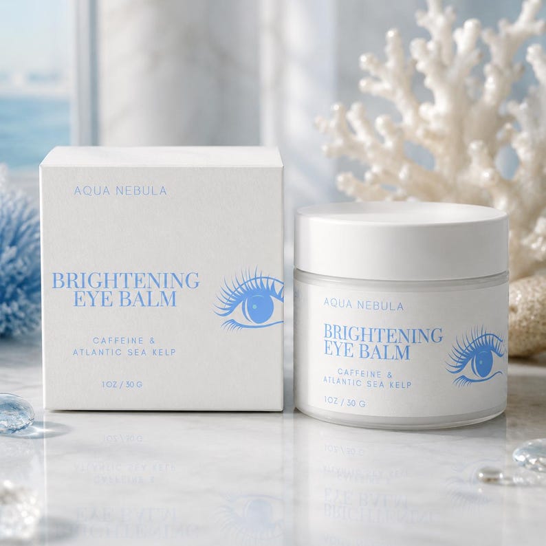 May include: A white square box and a matching cylindrical jar of Aqua Nebula Brightening Eye Balm. Both feature blue text reading Caffeine & Atlantic Sea Kelp and an eye graphic. The label indicates a net weight of 1 oz / 30 g for the product.