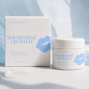 May include: A white square cardboard box and a matching white cylindrical jar of Aqua Nebula Nourishing Lip Balm with Shea Butter & Glacier Mist. Both items feature blue text and a blue lip icon, with a net weight of 0.5 oz / 15 g printed on each.