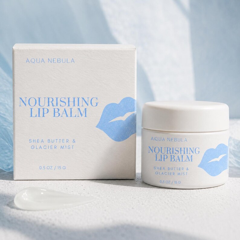 May include: A white square cardboard box and a matching white cylindrical jar of Aqua Nebula Nourishing Lip Balm with Shea Butter & Glacier Mist. Both items feature blue text and a blue lip icon, with a net weight of 0.5 oz / 15 g printed on each.