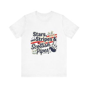 以下が含まれることがあります： 「Stars, Stripes & Scottish Pipes」の文字が入った白いTシャツ。星、ストライプ、アザミ、バグパイプのイラストがデザインされています。スコットランドとアメリカを愛する人のためのカジュアルなTシャツです。