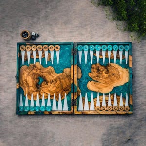 May include: A handcrafted backgammon set with a wooden playing surface and turquoise resin accents. The set includes wooden game pieces, dice, and a wooden dice cup. The board is open, ready for play, and sits on a neutral surface.