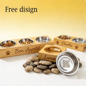 Puede incluir: Cuencos de madera para comida de mascotas con insertos de acero inoxidable. Un cuenco tiene el texto "Luna", otro "Charlie" y un tercero "Bon Appétit". Los cuencos están sobre un lecho de piedras. La imagen también incluye el texto "Free disign".