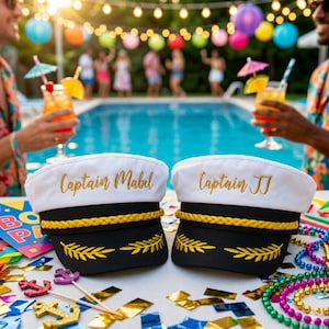 Peut inclure: Deux casquettes de capitaine blanches et noires avec une bordure en corde dorée brodée et des détails de feuilles dorées sur la visière. Le chapeau de gauche porte l'inscription Captain Mabel et celui de droite Captain JJ en lettres dorées.