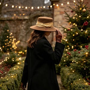 May include: A brown felt fedora hat featuring a wide, shimmering gold ribbon band with a small metallic buckle detail. The hat is worn with a long black coat and brown leather gloves, creating a structured and classic appearance.