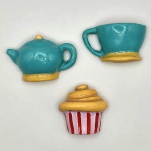 May include: A teal teapot, teacup, and cupcake set. The teapot and teacup have yellow bases. The cupcake has a yellow top and a pink and red striped base. The set is likely for decorative purposes.