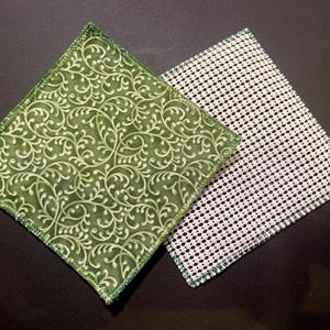 May include: Two square coasters. One is green with a white floral pattern, the other is white with a black dot pattern. Both have green stitched edges. The coasters are likely made of fabric and are designed to protect surfaces from heat and moisture.