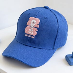 Puede incluir: Una taza de cerámica blanca con un asa negra y el texto "But First, Coffee" en negro, con una fuente de estilo manuscrito. La taza está sobre una superficie blanca.