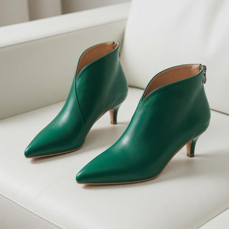 May include: A pair of emerald green ankle boots with pointed toes and a low heel. The boots have a V-shaped cut at the front and a zipper at the back. The shoes are made of a smooth, shiny material.